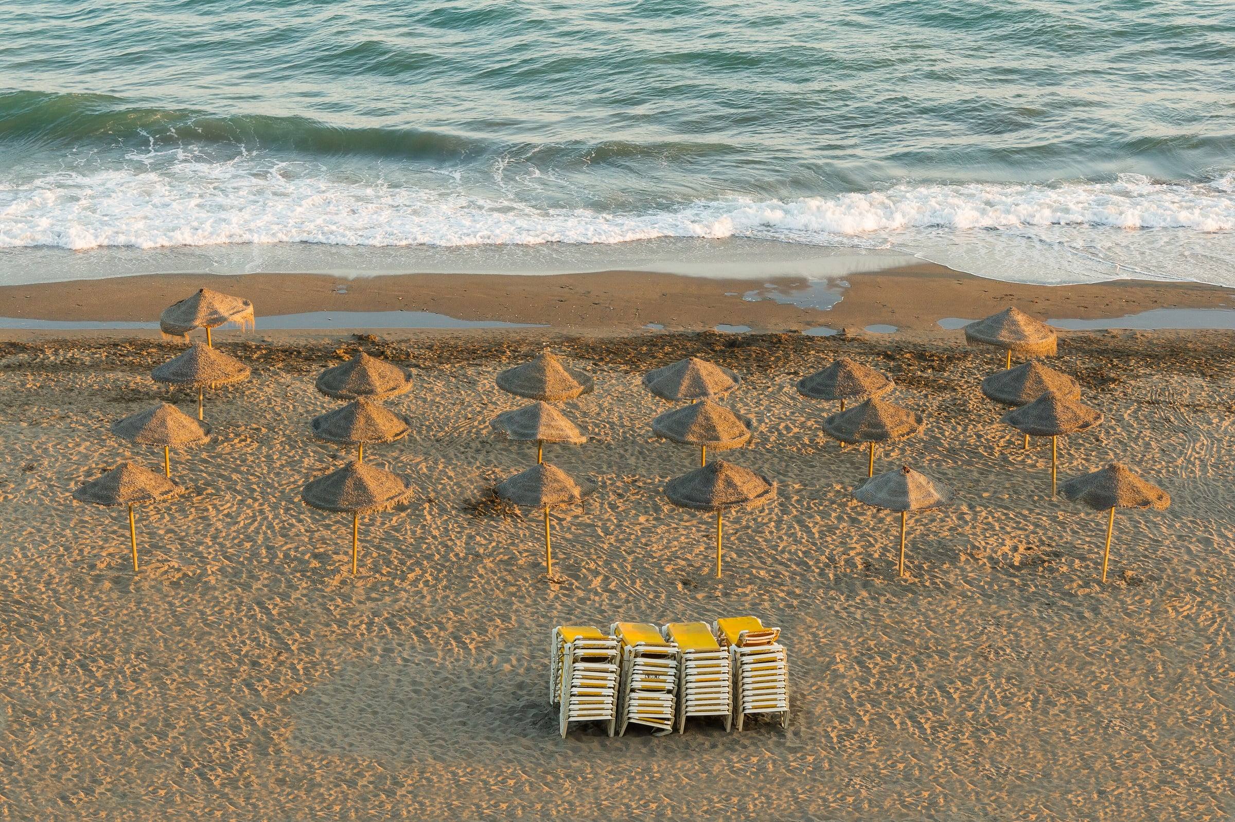 Straw parasols and stacked sun loungers on an empty beach at Rincón de la Victoria, near Málaga, in evening light