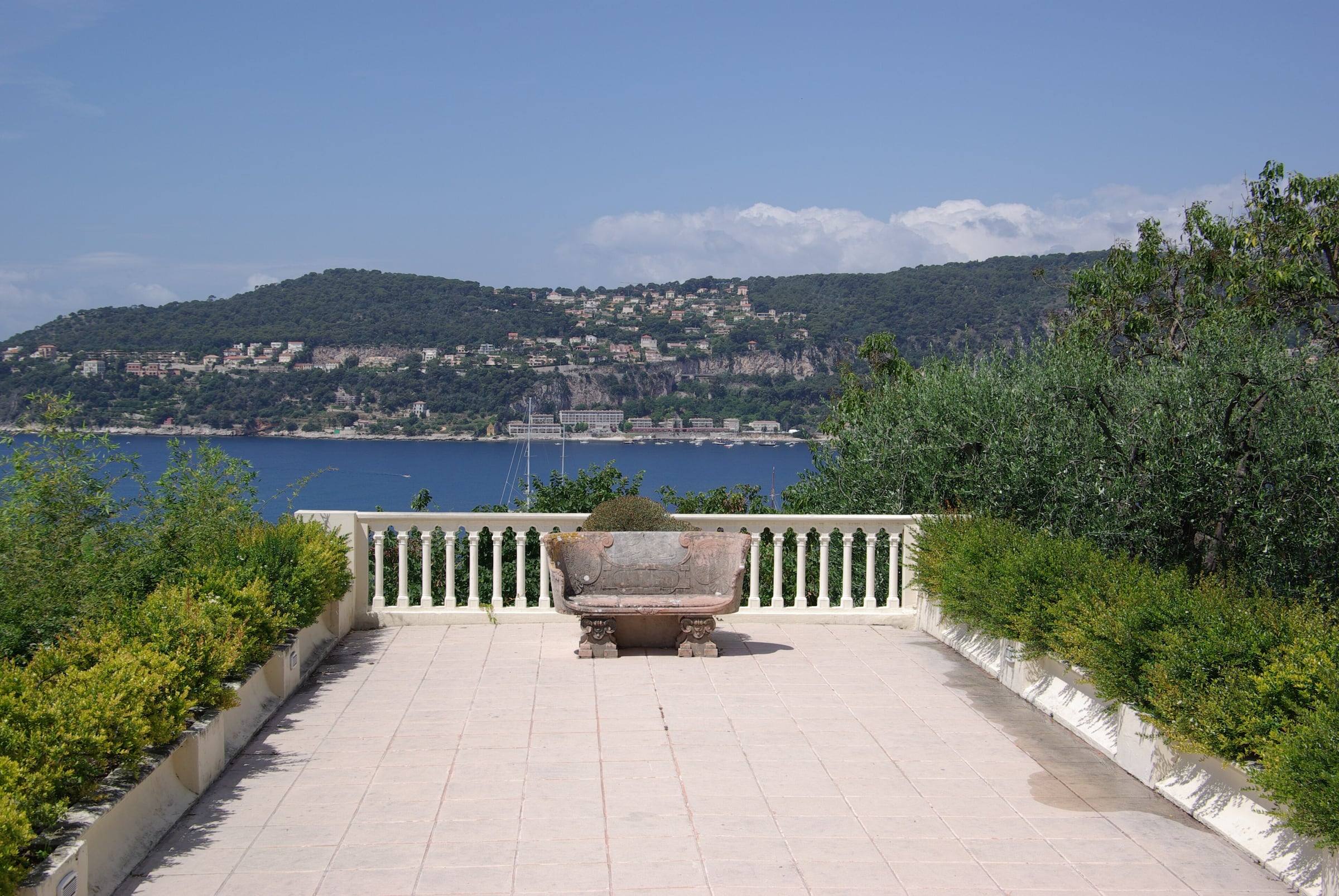 A garden terrace with a stone bench, looking across the bay towards Villefranche-sur-Mer